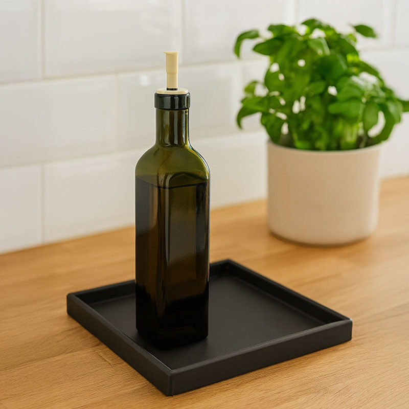 Sort bakke fra Sej Design med olivenolieflaske og basilikum på egetræs bordplade i lyst nordisk køkken.