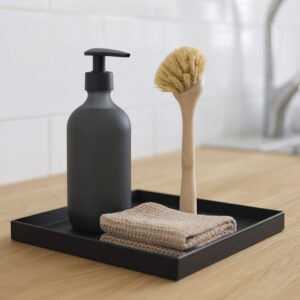 Sort bakke fra Sej Design med opvaskeflaske, opvaskebørste og strikket karklud på lys egetræs bordplade i nordisk køkken.